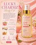 A bottle of Lucky Charmz Body Oil by Gandi Shop is displayed on a pink satin fabric next to a lit candle, with decorative flowers and a clover charm. The left side features a detailed scent notes graphic.