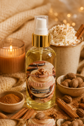 A bottle of body oil from The Candi Shop, styled with cinnamon sticks, nutmegs, a lit candle, and a cup of whipped cream in a cozy, warm setting.